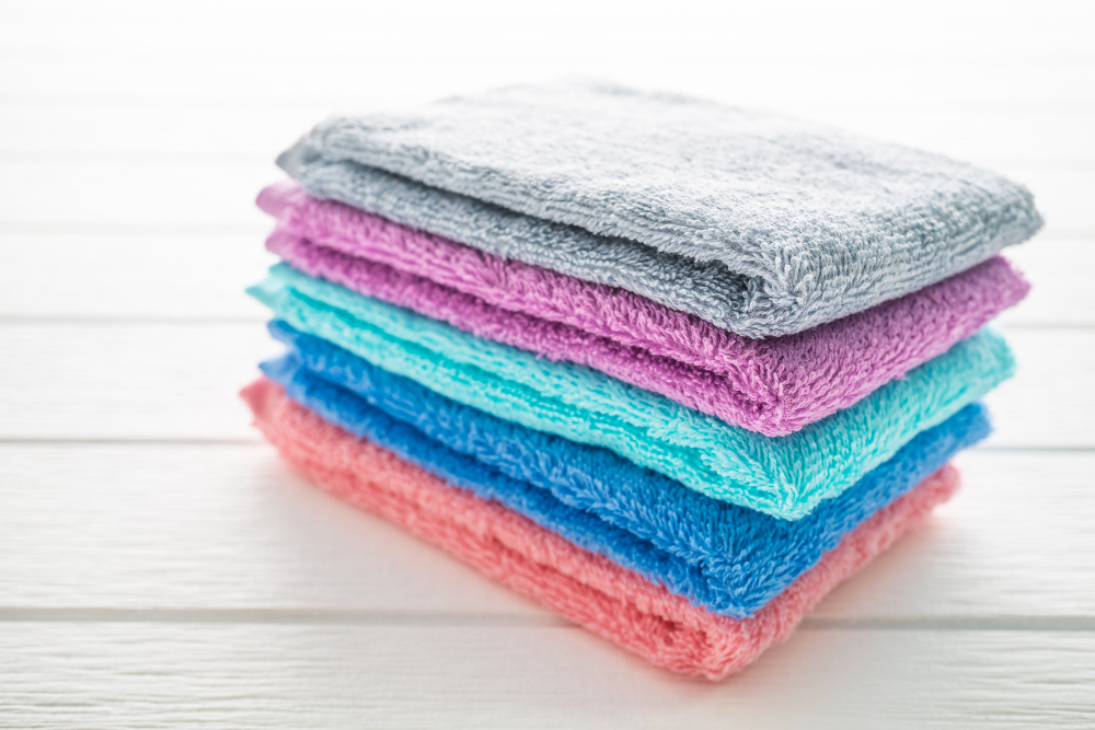 A neatly stacked pile of colorful towels in gray, purple, blue, and pink shades on a white wooden surface.